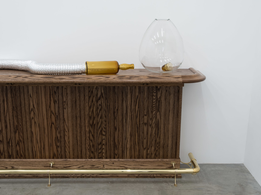 Detailed installation view of AKI SASAMOTO’s Past in a Future Tense, Bar End, 2019, hand-blown glass, whiskey glass, HVAC system, centrifugal fan, speed control, red oak, foot rail, coat hooks, and umbrella, 381 × 536 × 50.8 cm, at “Past in a Future Tense,” Bortolami Gallery, New York, 2019. Courtesy the artist and Bortolami Gallery.