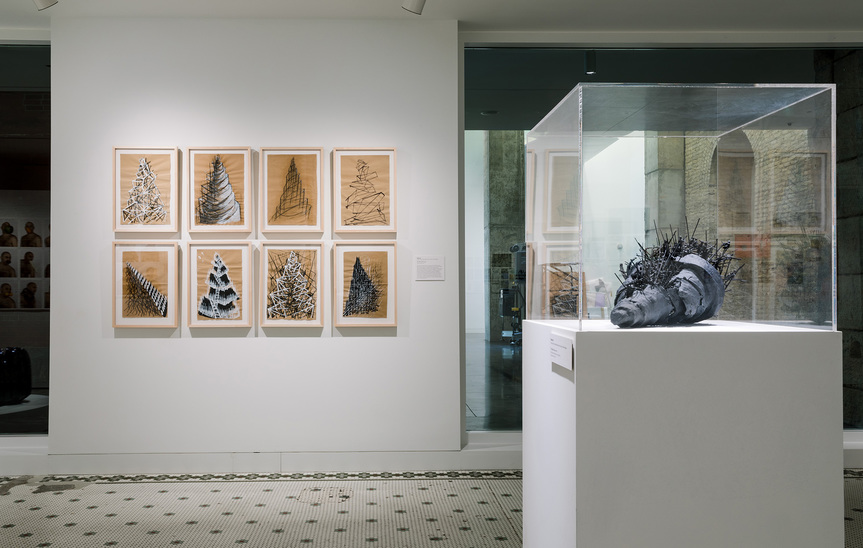 Installation view of WALID SITI’s (left) The Tower Series, 2016, acrylic and crayon on paper, eight drawings, 42 × 28 cm each; and (right) The Black Tower, 2016, plastic figurines, plaster, acrylic, and twigs, 40 × 50 × 40 cm, at “History is Not Here: Art and the Arab Imaginary,” Minnesota Museum of American Art, 2019.