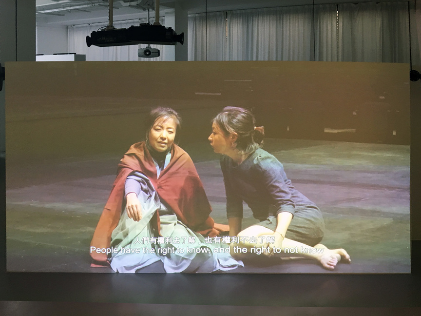 SHEN XIN’s four-channel video Provocation of the Nightingale (2017) is played across three sections of screens programmed to start after the completion of the previous video. The whole experience, encompassing four videos, takes 53 minutes. Here in the first video, two women discuss science and faith on a stage.