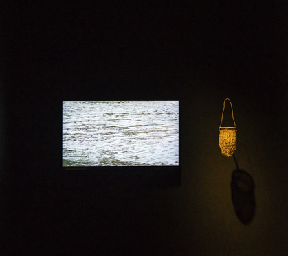 Installation view of JULIE GOUGH’s Crime scene (Survivor), 2019–20, tereena (basket), flag iris: Diplarrena moraea, “blueberry": Dianella tasmanica, river reed: Schoenoplectus pungens, pale rush: Juncus pallidus, video edited by Angus Ashton: 18 min 31 sec, at “Rite of Passage,” QUT Art Museum, Brisbane, 2020. Photo by Louis Lim. Courtesy the artist.